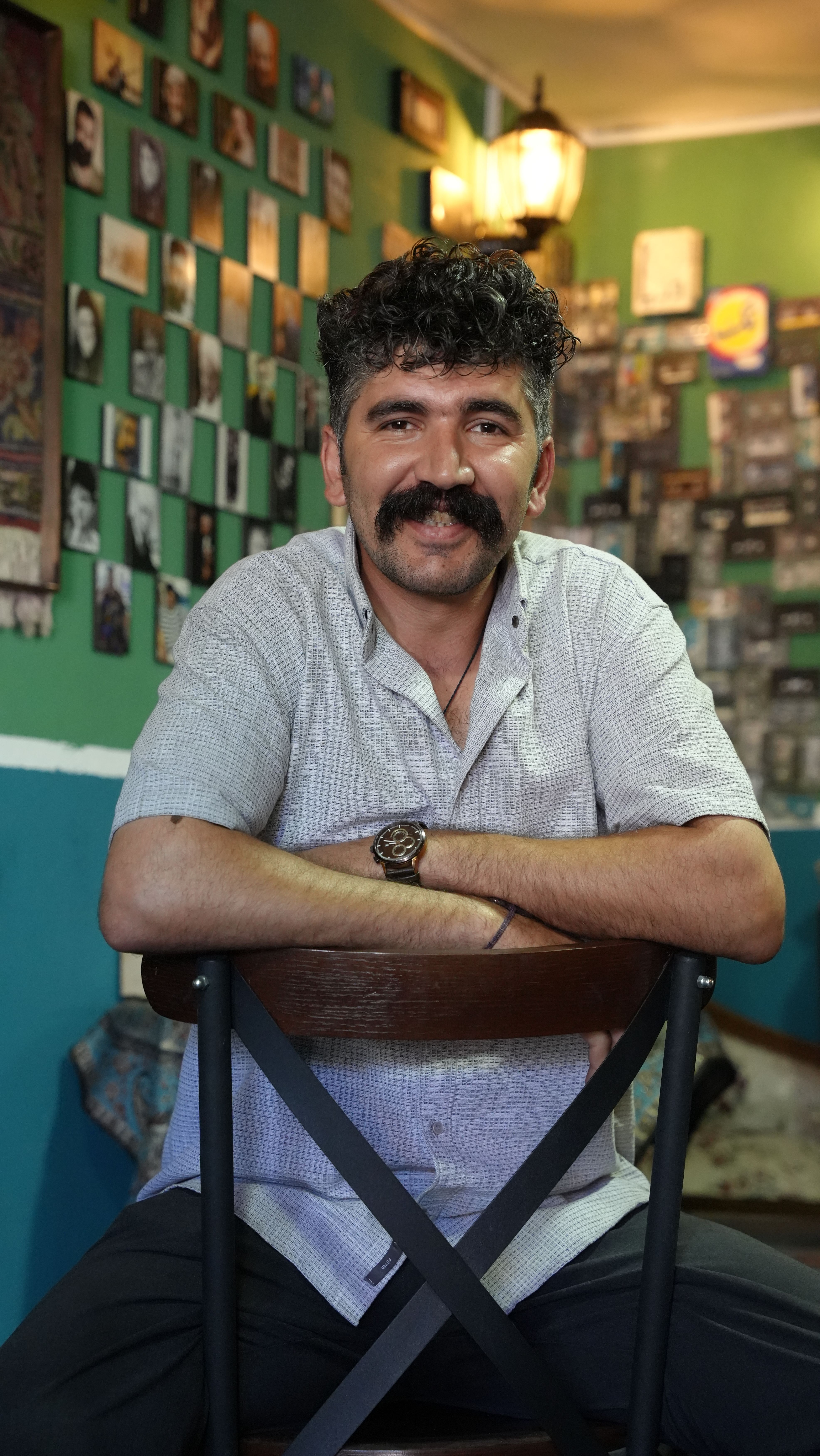 Portrait of a smiling man in a charming Iranian cafe with a colorful photo wall backdrop.