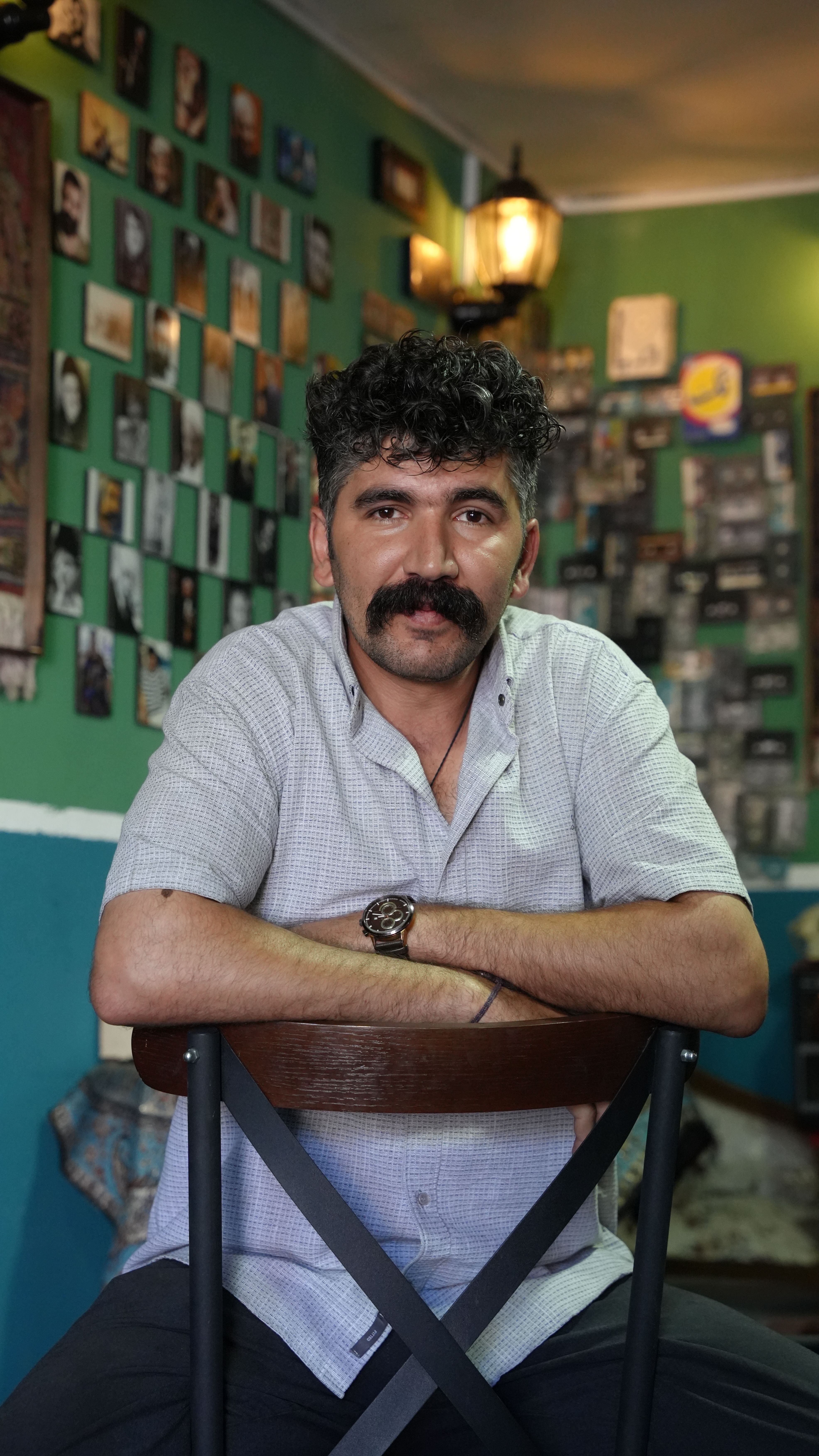 Middle-aged man sitting in a cozy, traditional Iranian café with photo-adorned walls.
