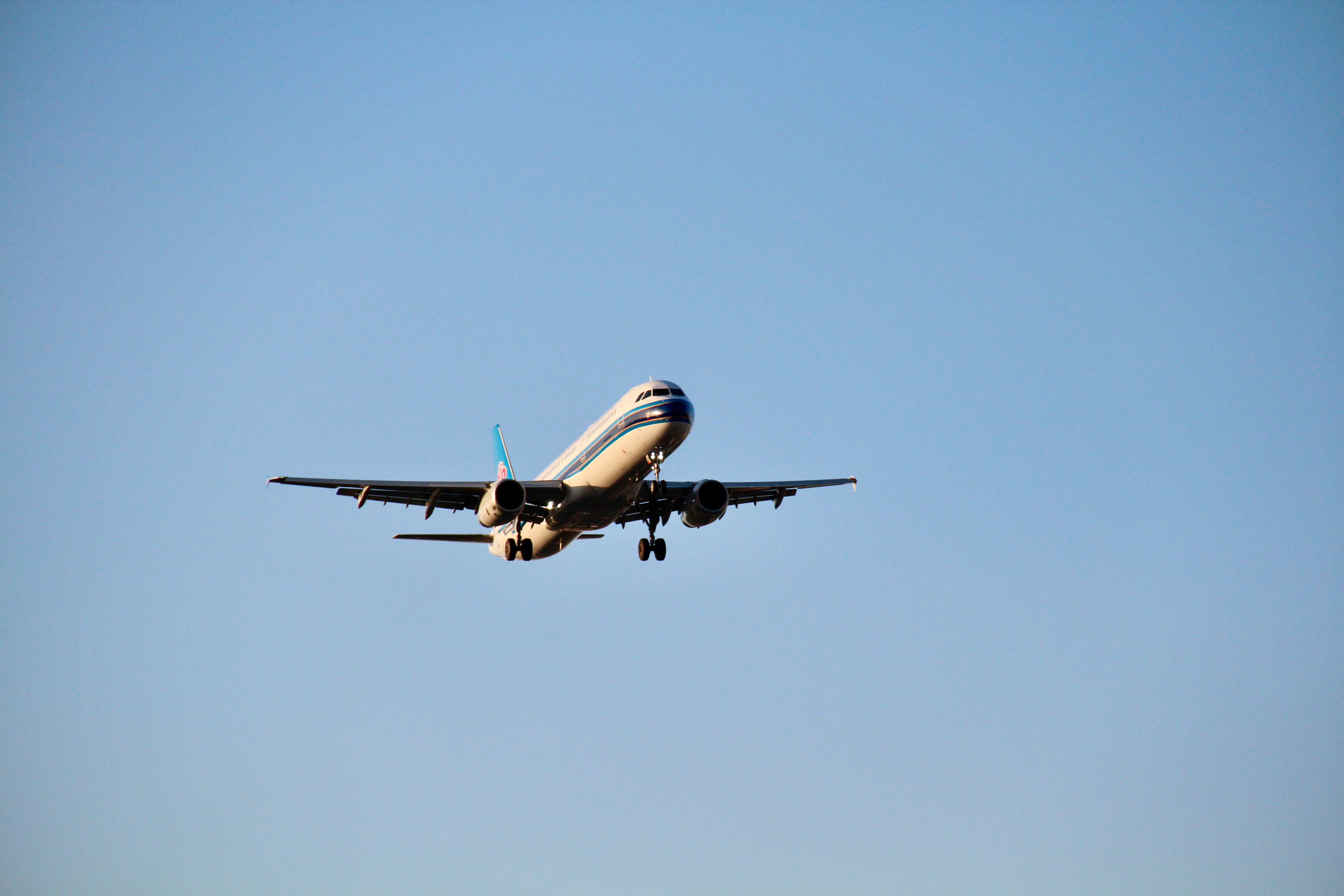 A commercial airplane approaches for landing under a clear blue sky, captured from below.