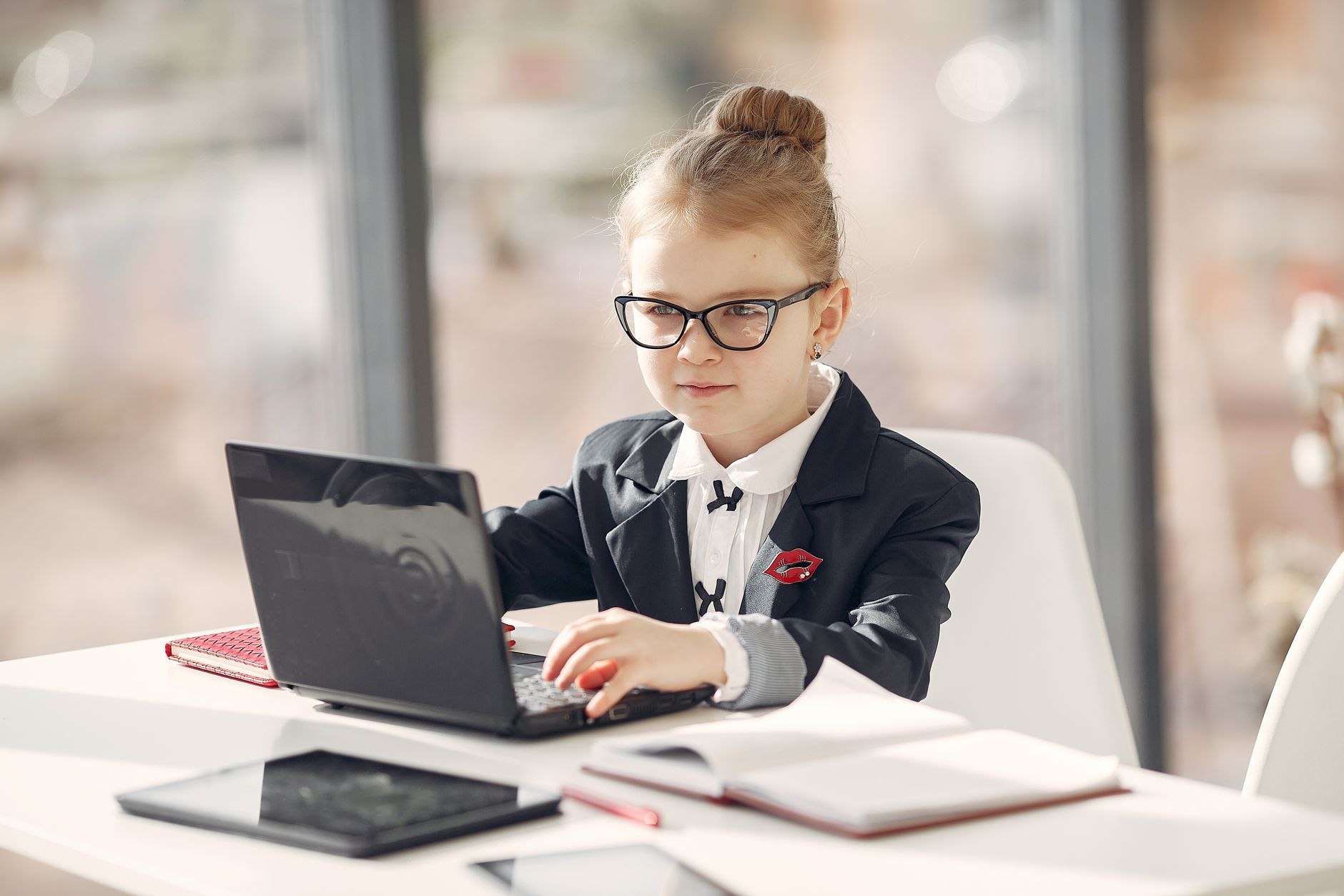Positive preschool employee in formal clothes and eyeglasses having online conversation with client while using laptop in light office