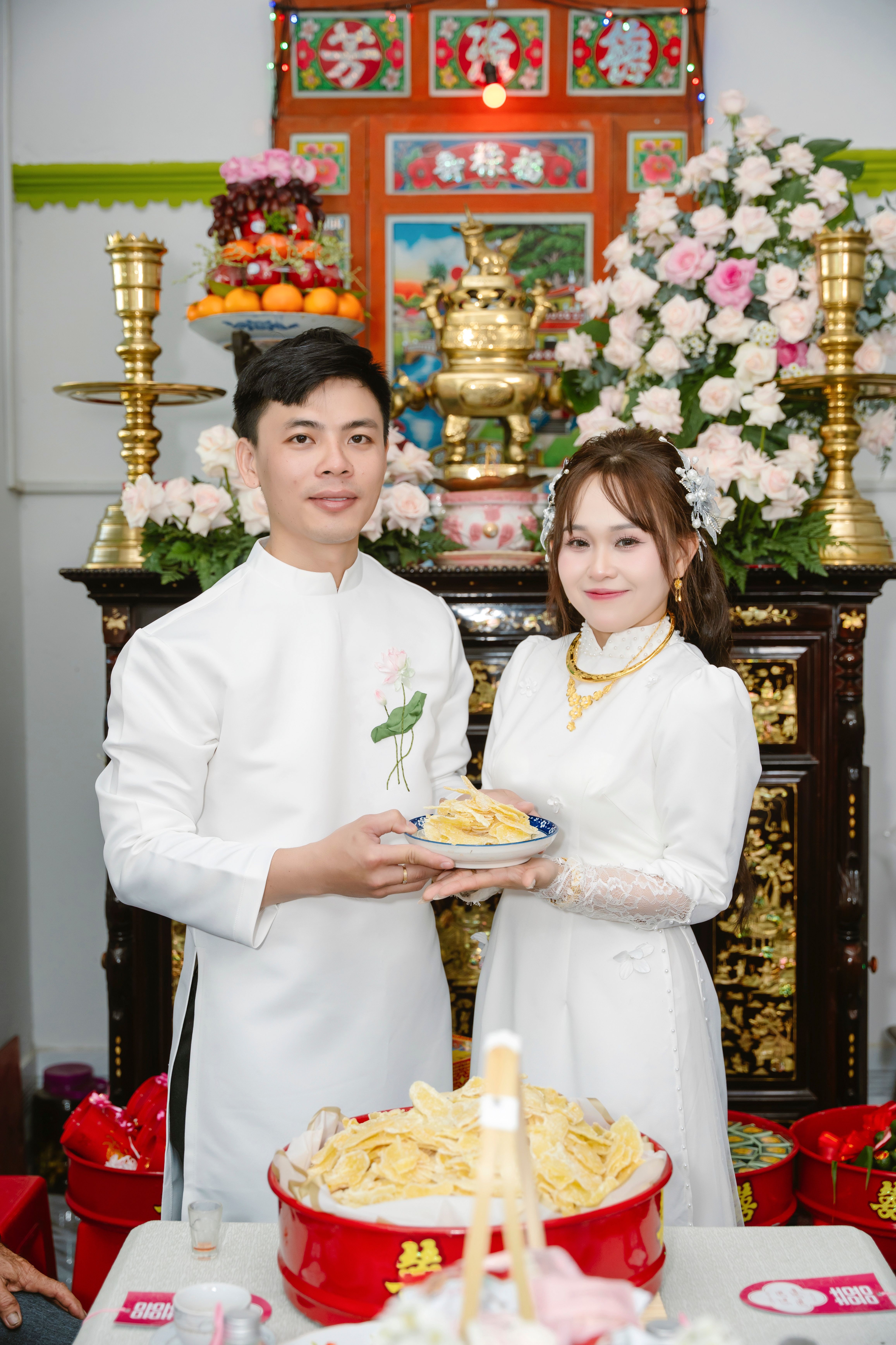 A couple in traditional attire during a Vietnamese wedding ceremony with ornate decor.