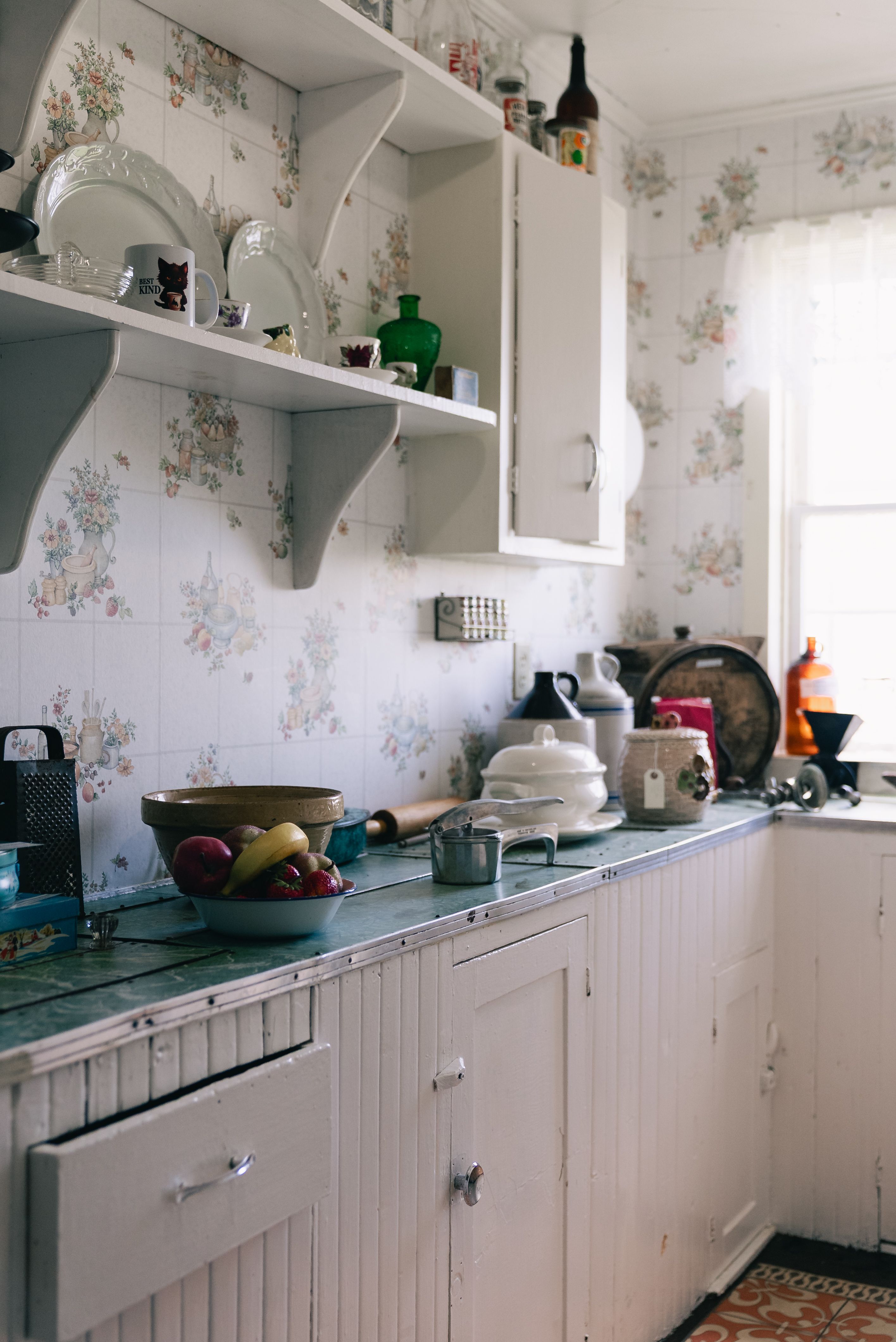 Dated kitchen with floral wallpaper and older cabinets