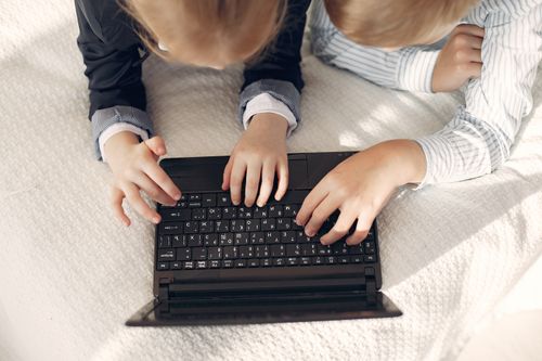 Free From above of crop boy and girl in formal clothes browsing netbook while resting on cozy bed during free time at home Stock Photo