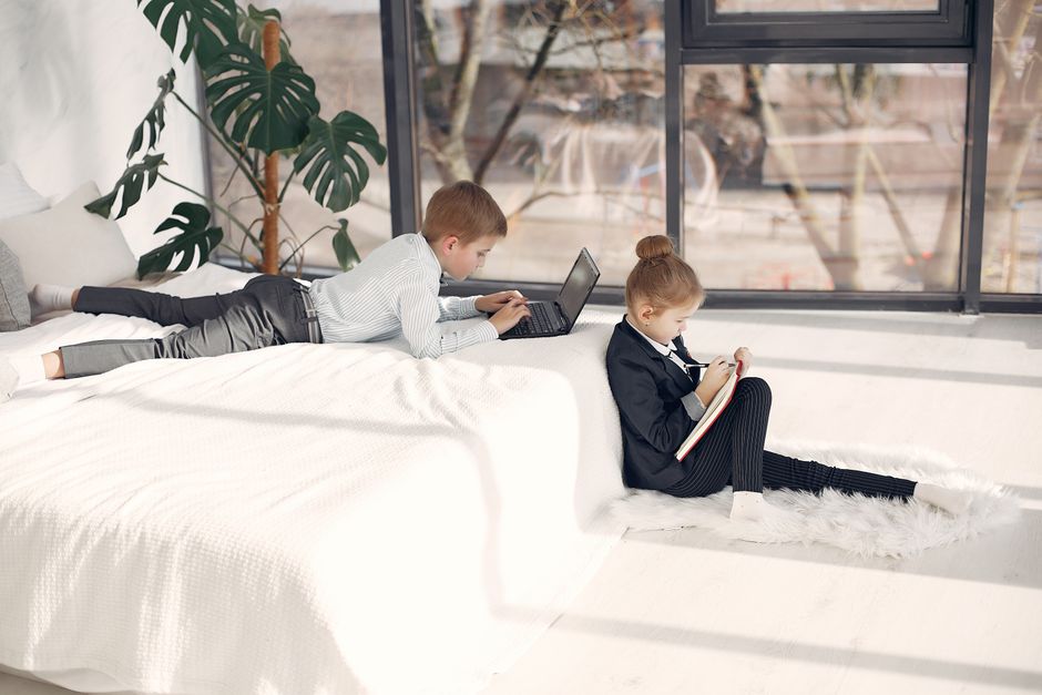 Dos niños vestidos formalmente, participando en trabajo y aprendizaje en casa con una laptop y un cuaderno.