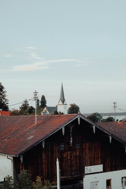 View of a traditional Bavarian village with a church steeple and rustic rooftops in Gstadt am Chiemsee, Germany.