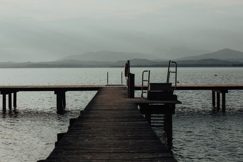 Free Serene view of a wooden pier stretching into Chiemsee Lake in Bavaria with distant mountains. Stock Photo