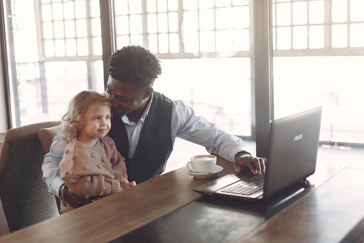 Cheerful Young African American Man Looking After Little Girl In Cafe Using Laptop