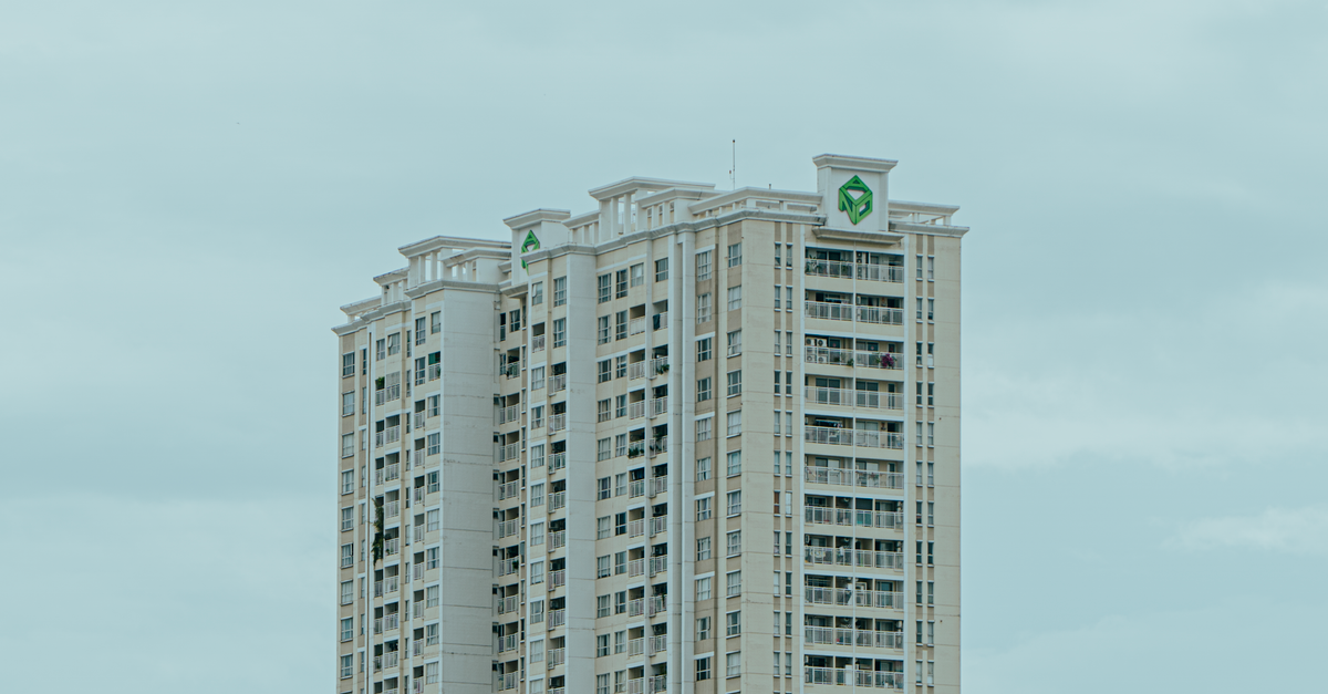 A tall modern apartment building stands against a cloudy sky, showcasing urban architecture.