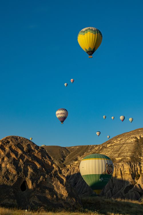 Free Colorful hot air balloons soar over Cappadocia's stunning rock formations under a clear blue sky. Stock Photo