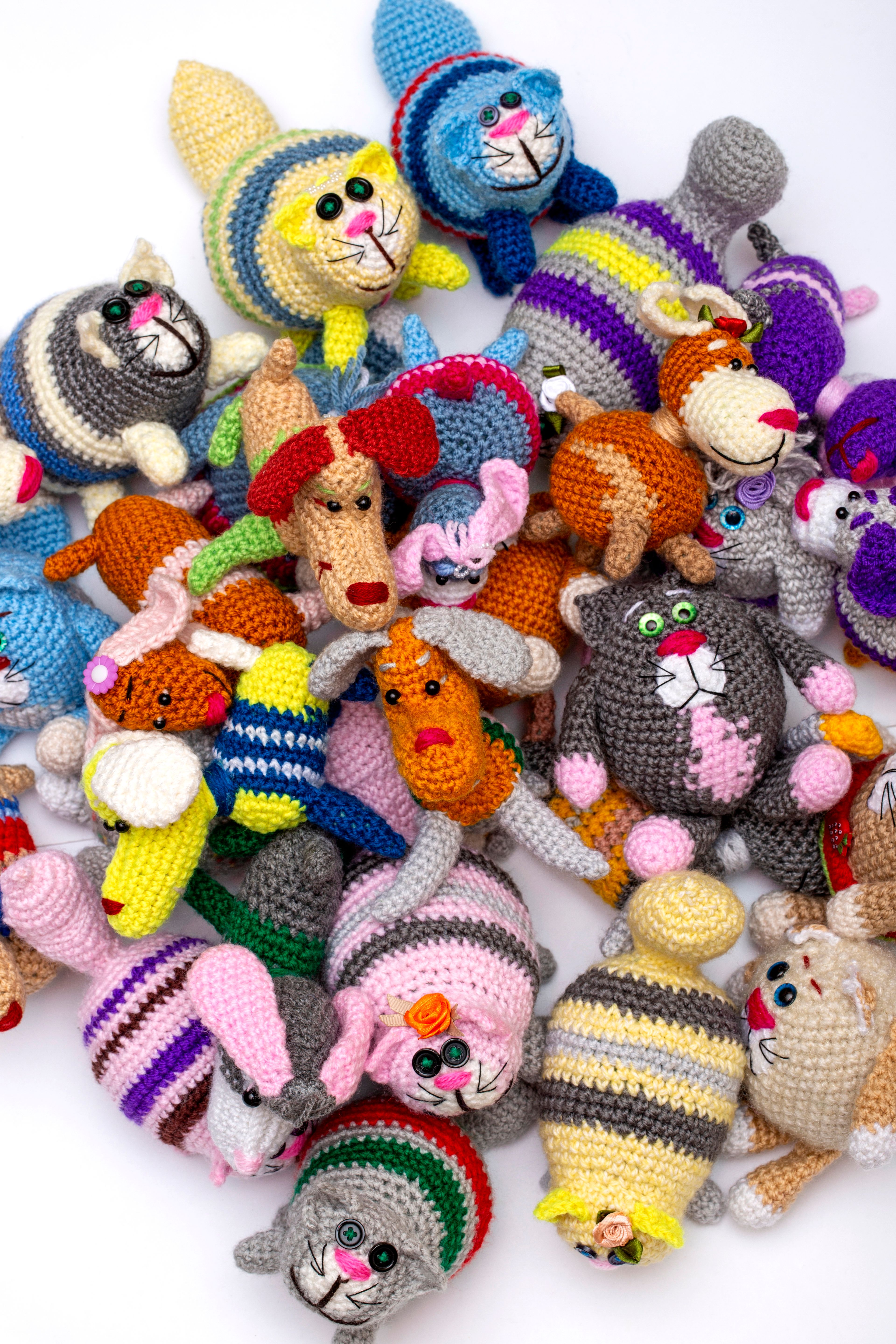 A vibrant collection of handmade crochet animal toys with diverse colors and patterns displayed on a white background.
