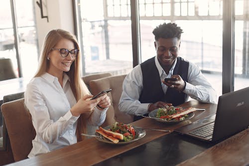 Cheerful diverse colleagues using phones during business lunch in cafe