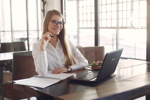 Smiling woman working on laptop and notebook in a bright café environment.
