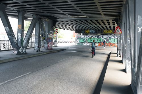 Free Cyclist rides under a graffiti bridge in Hamburg, showcasing urban art and architecture. Stock Photo