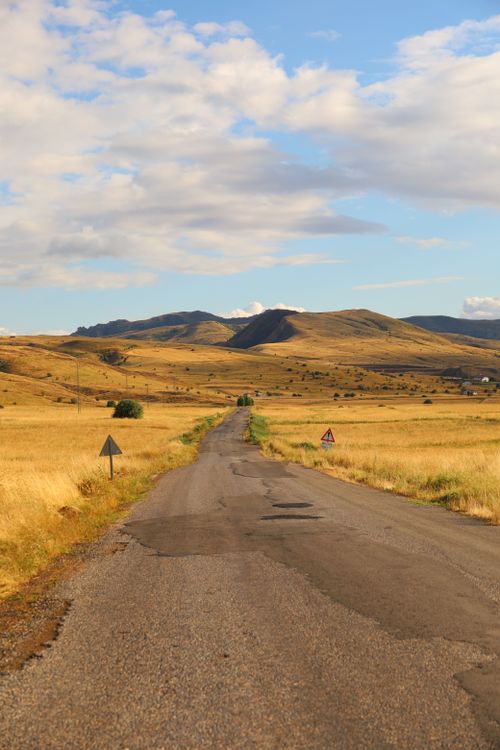 Free Empty rural road stretches through a golden field under a bright, partly cloudy sky at sunset. Stock Photo