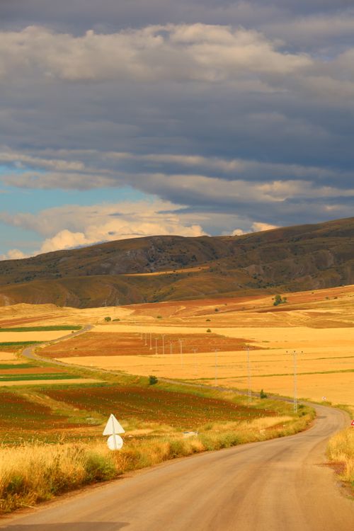 Free A winding road leads through colorful fields and hills under a dramatic sky. Stock Photo