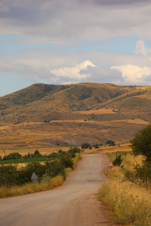 Free A picturesque rural road winding through golden hills under a partly cloudy sky. Stock Photo