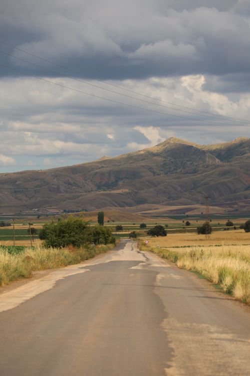 Free Discover a tranquil countryside road leading towards distant mountains under a cloudy sky. Stock Photo