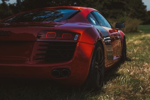 Free Stunning red sports car showcasing sleek design and luxury against a grassy backdrop. Stock Photo