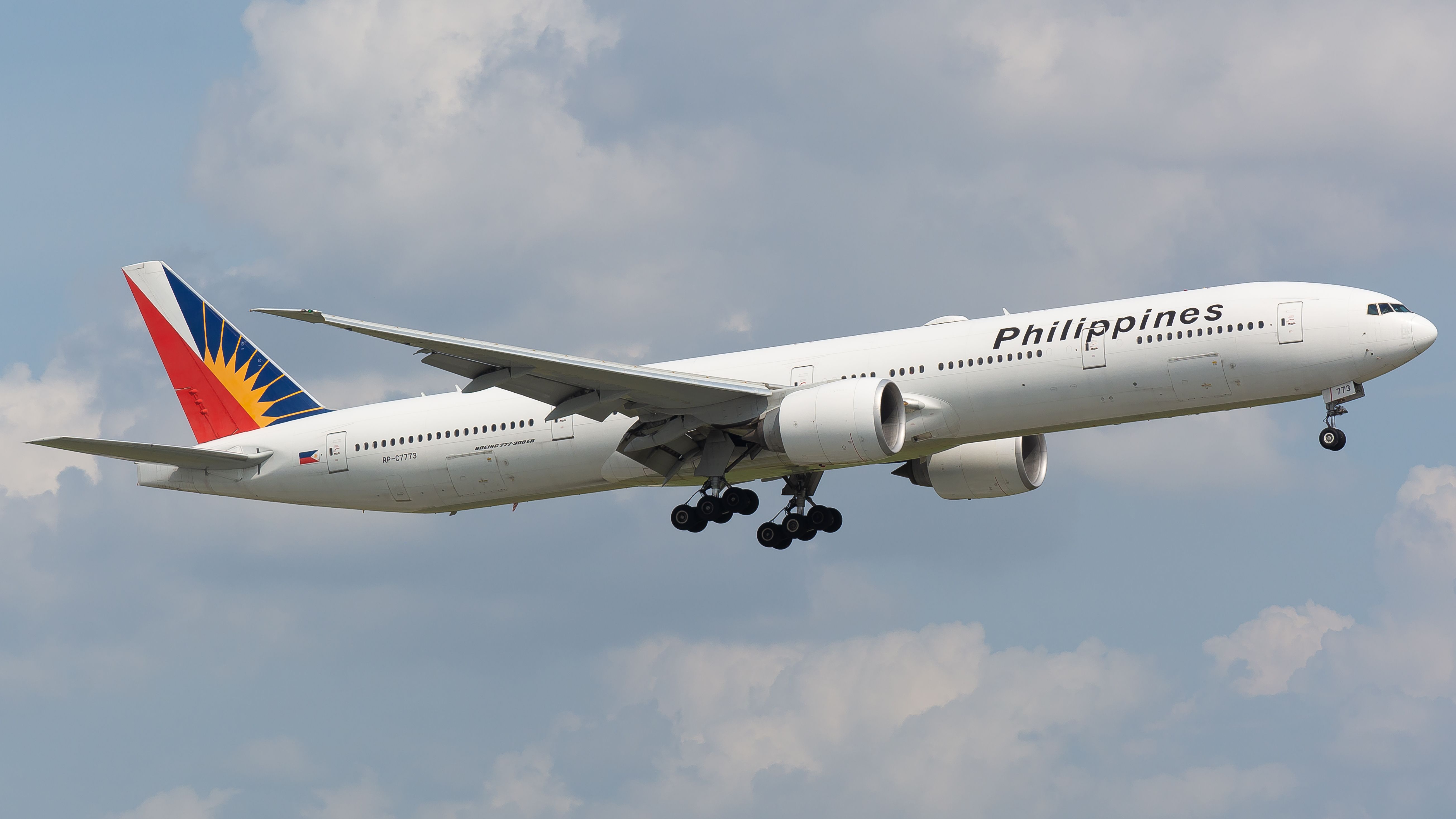 A Boeing 777 airplane of Philippine Airlines flying against a blue sky with clouds in daytime.