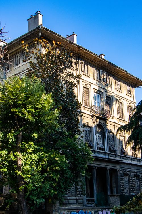 Free A vintage European building surrounded by vibrant green trees under a clear blue sky. Stock Photo