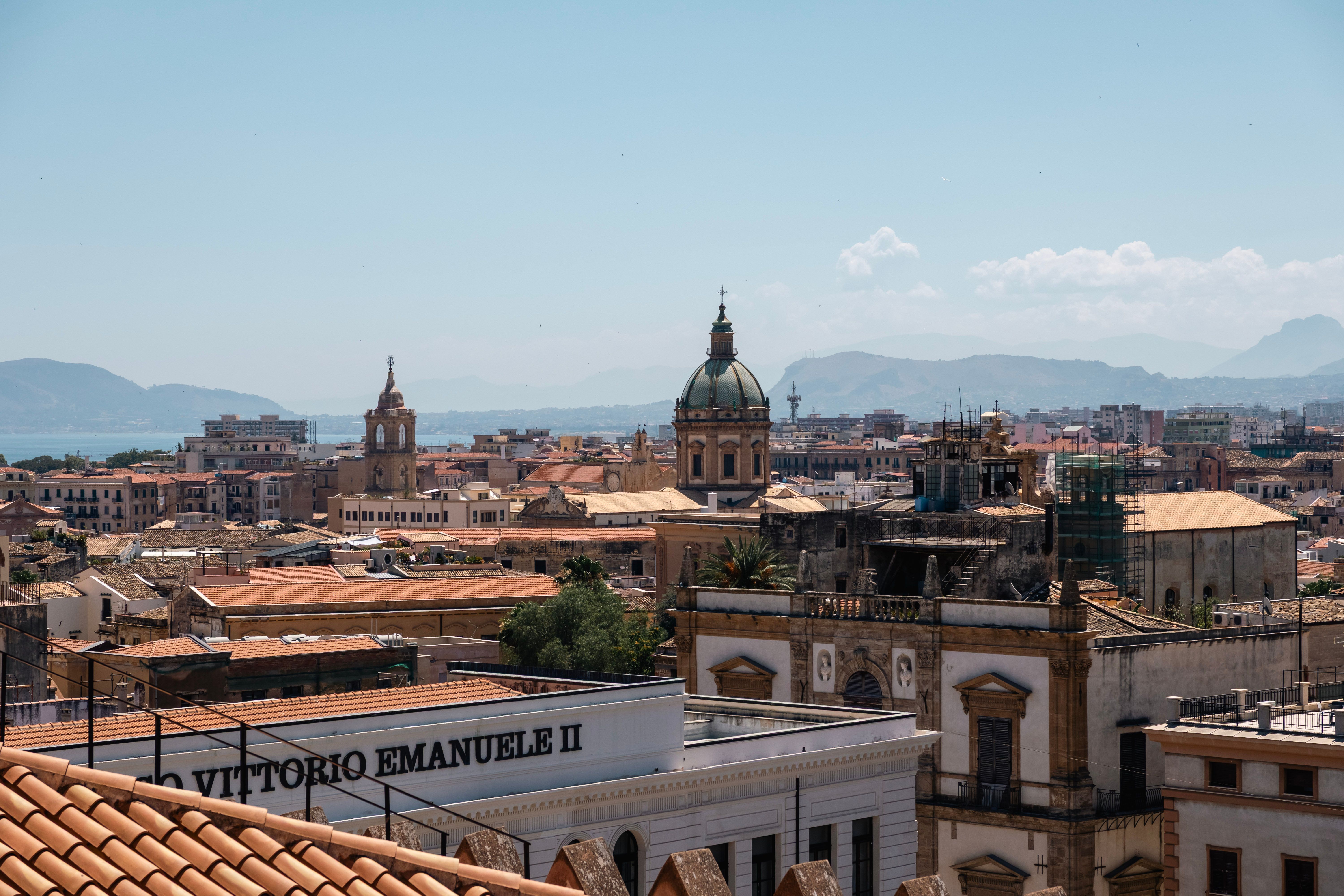 Captivating view of Palermo's historic architecture against a mountainous backdrop under a clear sky.