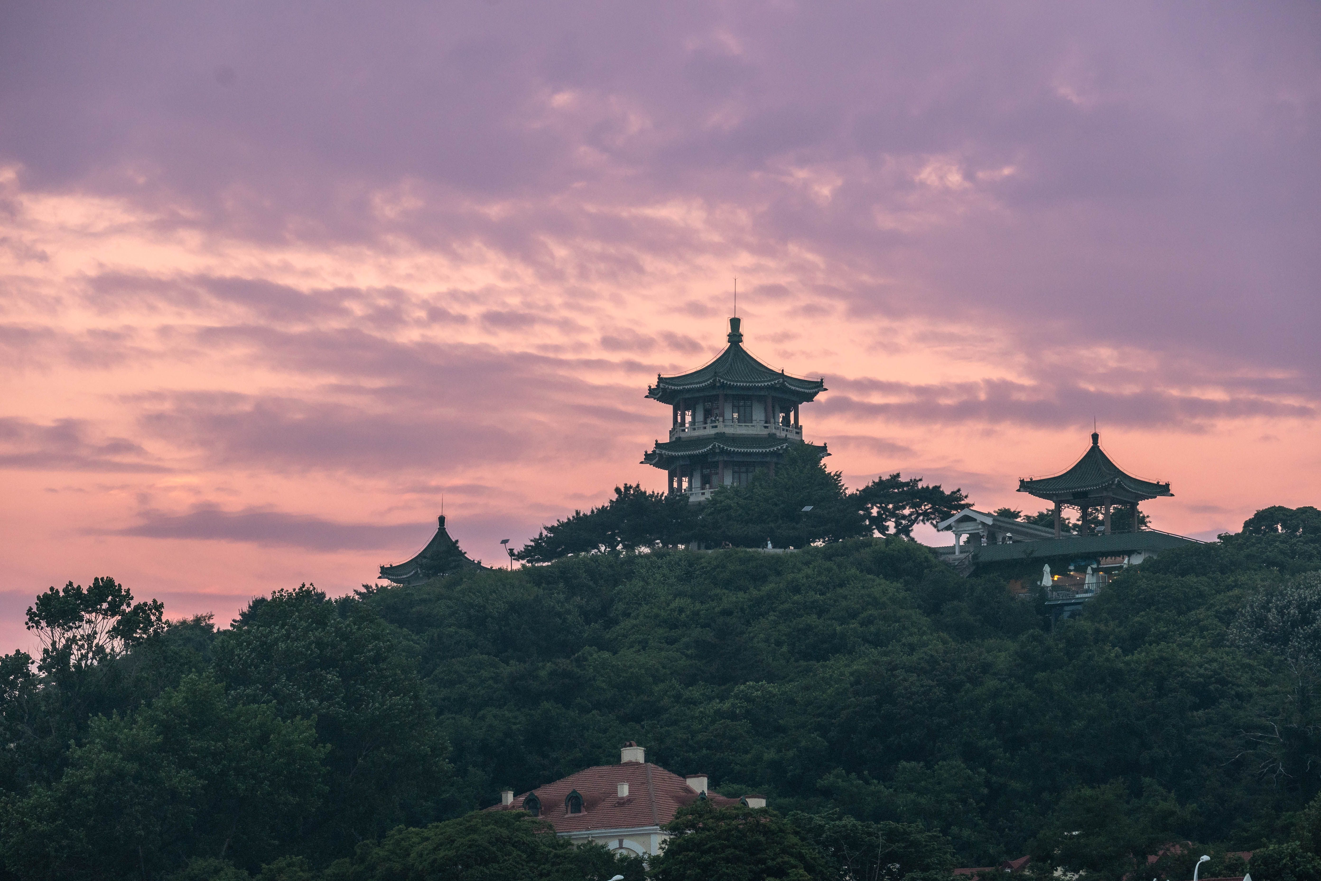 A beautiful pagoda stands atop a hill against a pastel dusk sky, surrounded by lush greenery.