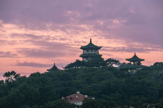 A beautiful pagoda stands atop a hill against a pastel dusk sky, surrounded by lush greenery.