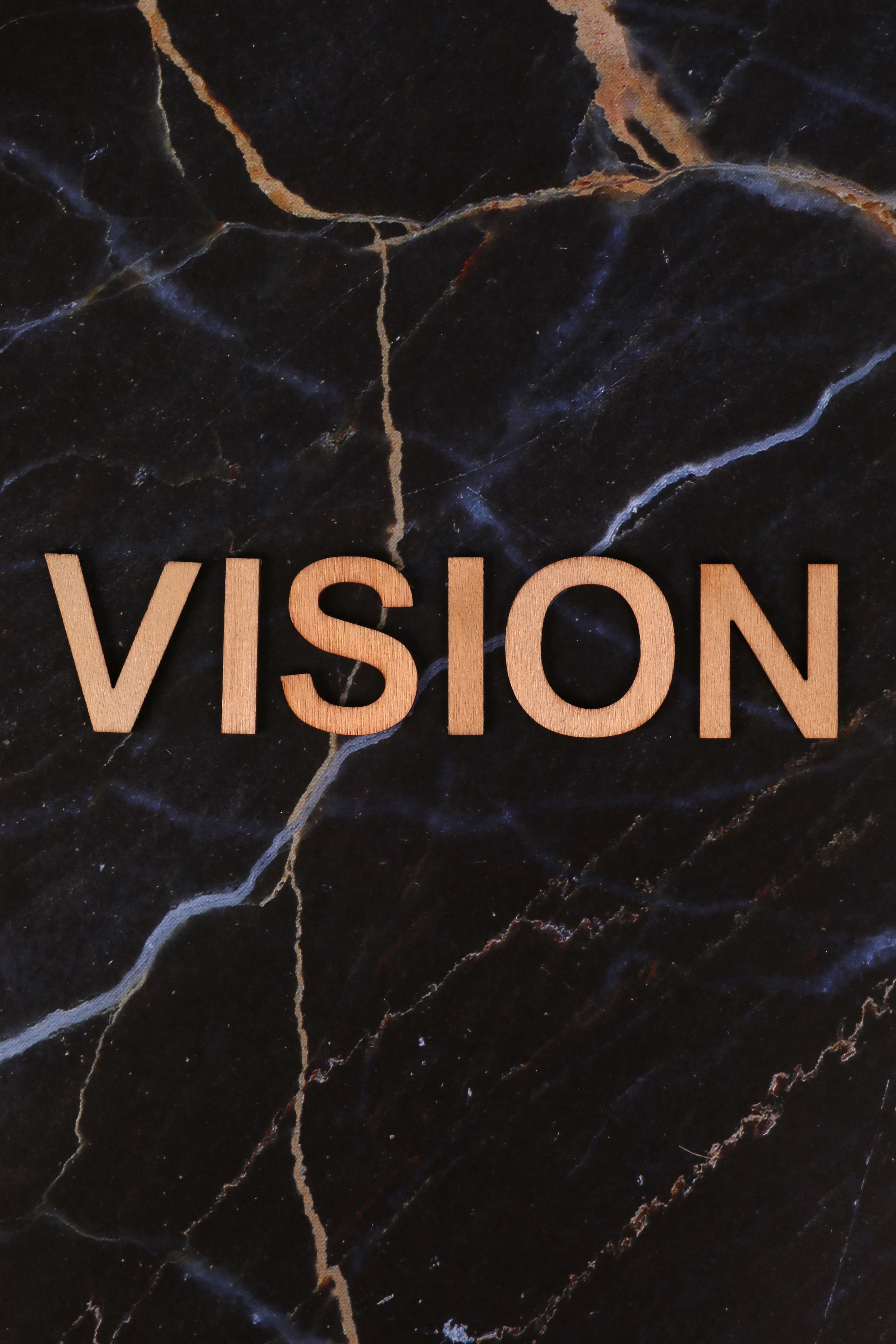 Wooden letters spelling 'VISION' on a dark marble surface, inspiring creativity.