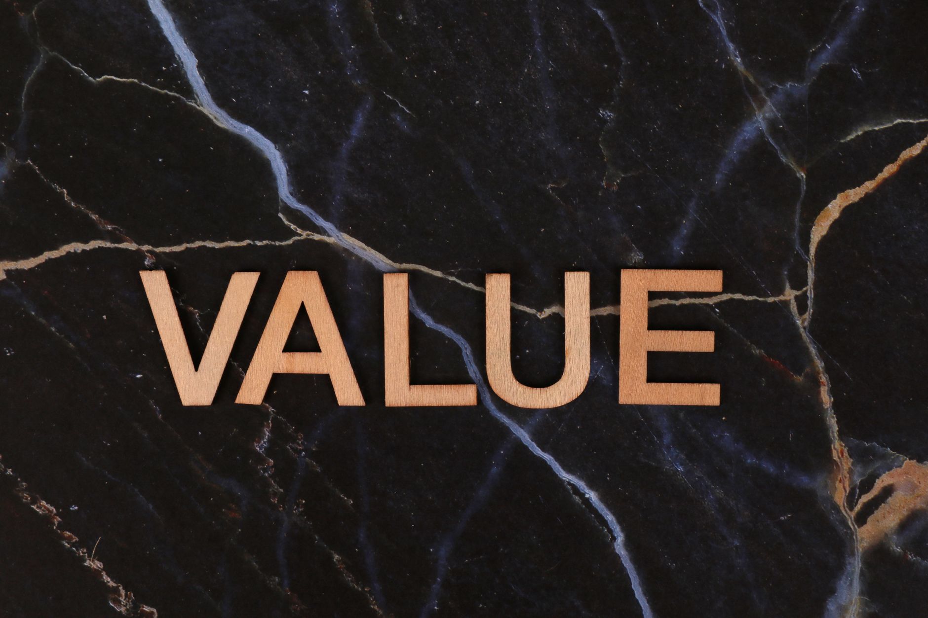 A close-up of wooden 'Value' letters placed on a dark marble background, emphasizing texture and concept.