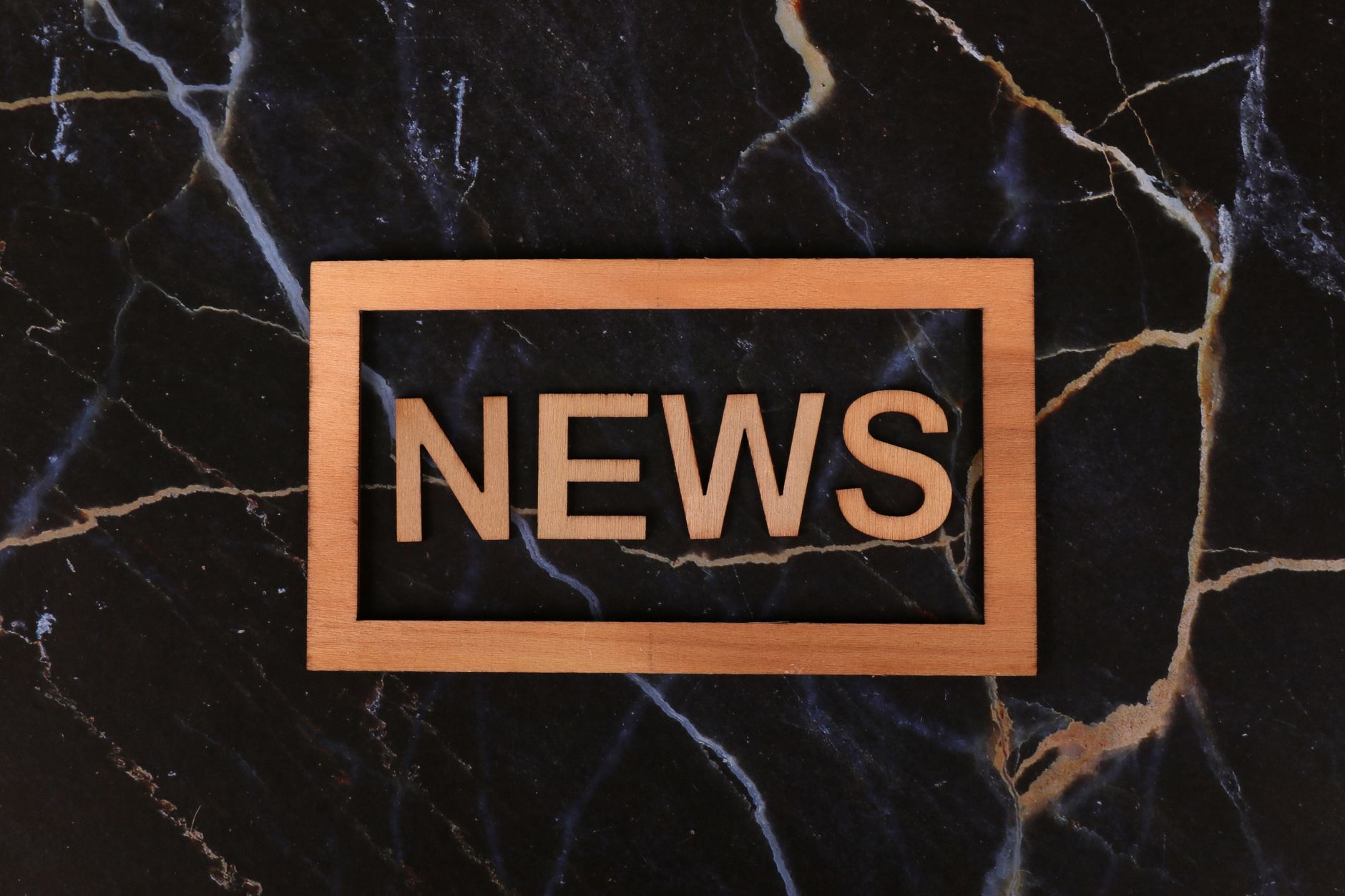 Wooden text of 'news' outlined on a dark, marbled surface, creating a striking contrast.