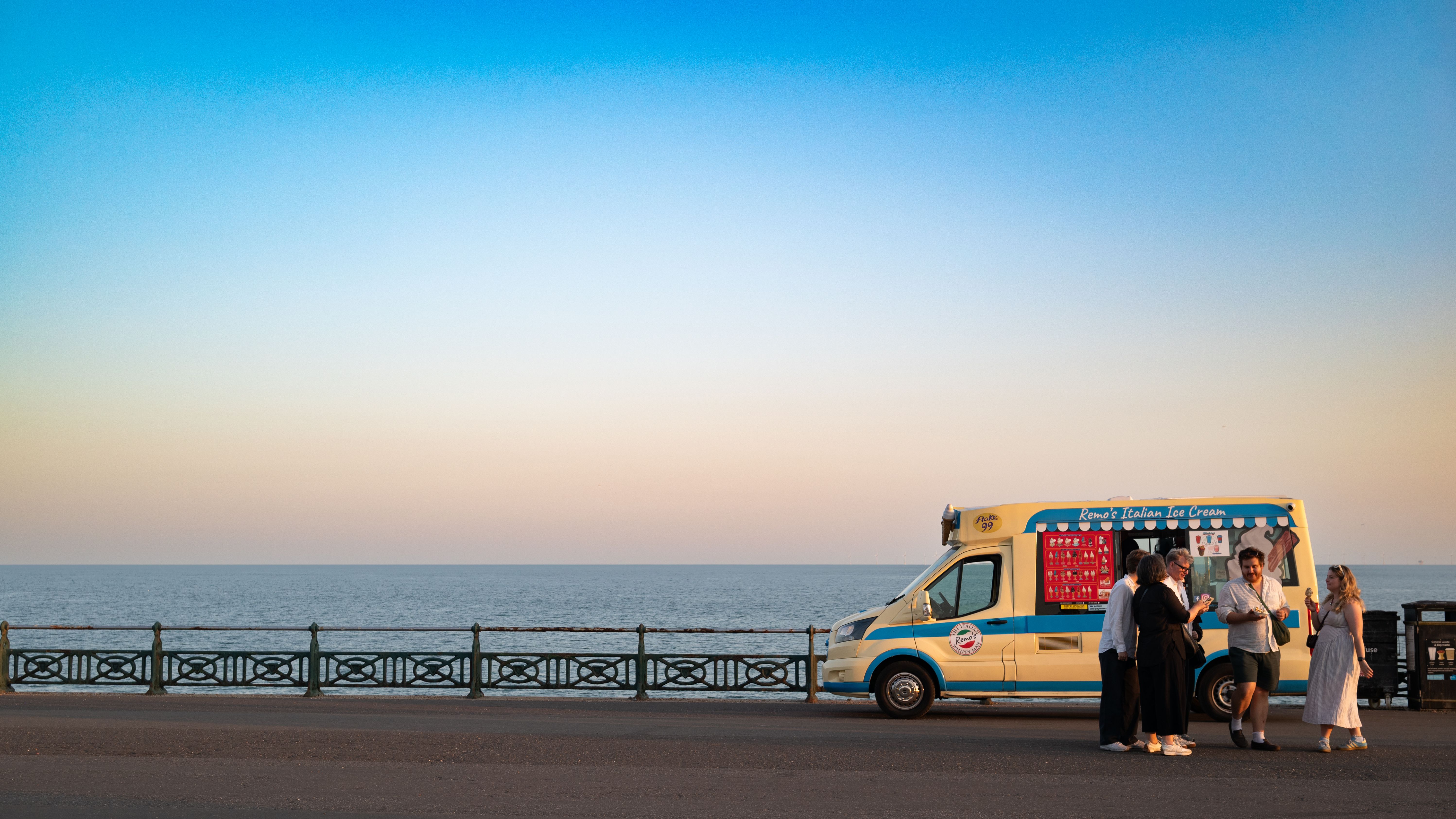 Group enjoys ice cream by a truck on Brighton's seaside during sunset.