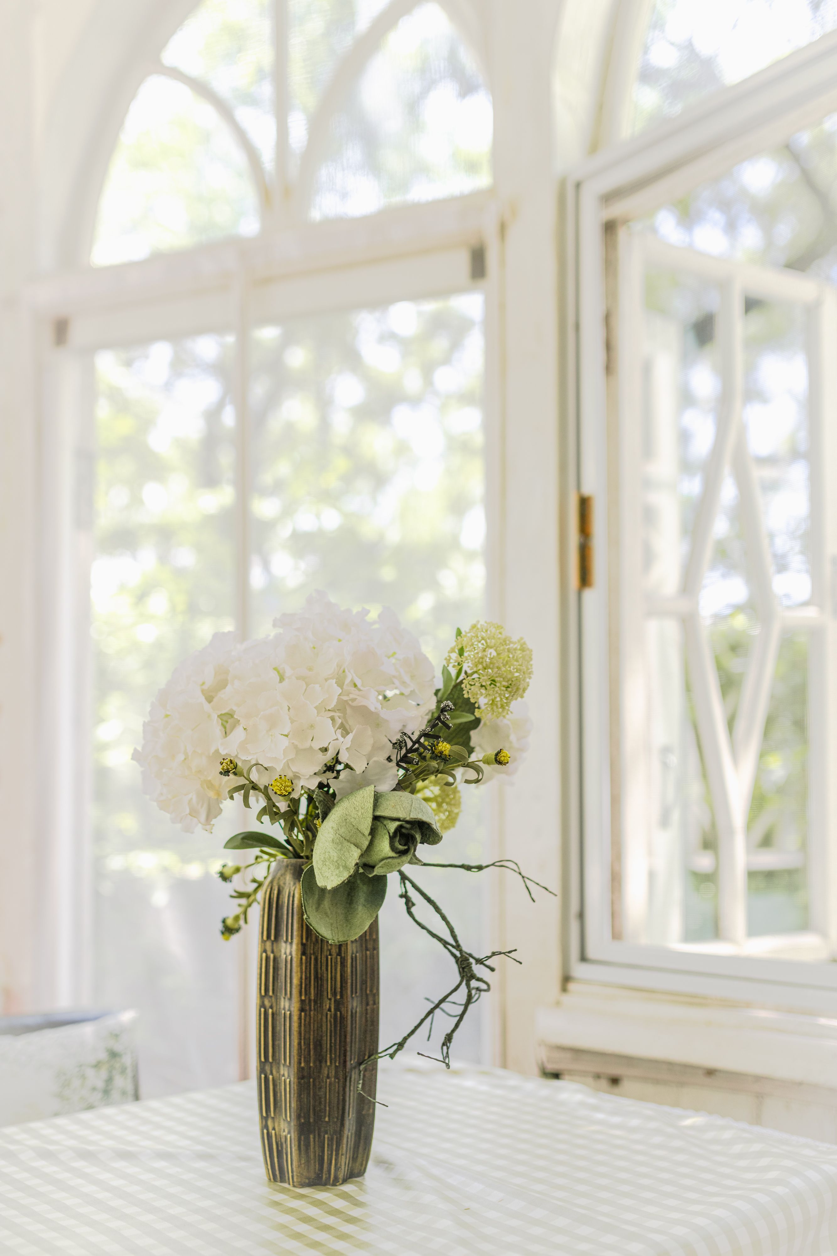 Beautiful white flowers in vase on table by open window, bright sunlight.