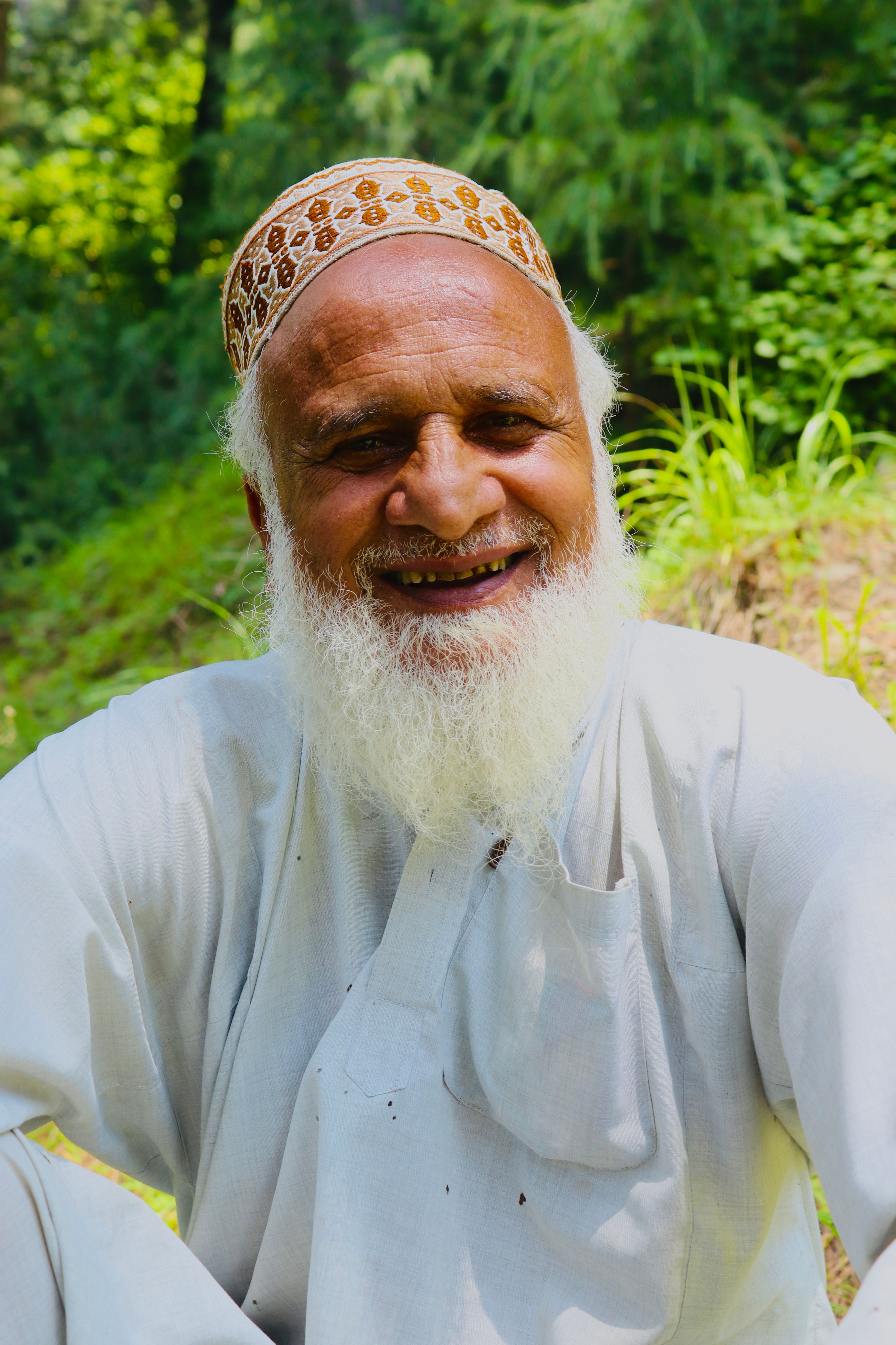 Portrait of a smiling elderly man with a white beard, seated outdoors against a vibrant green background.
