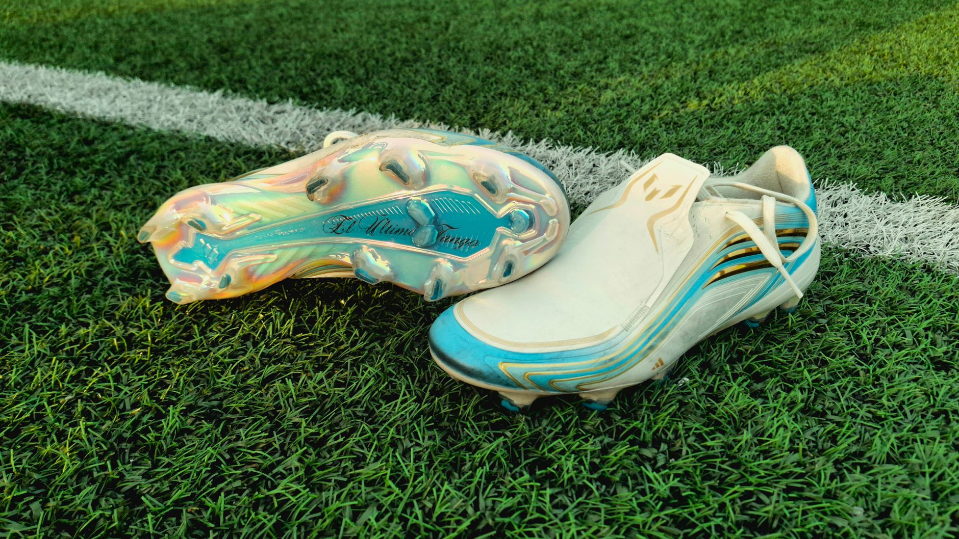 seven football cleats arranged by price on a wooden bench overlooking a youth training field