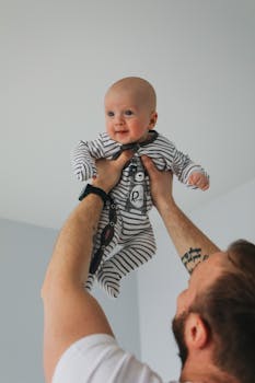 一位快乐的父亲在室内抱着他身穿条纹连体衣、面带微笑的婴儿，捕捉到了温馨的亲子时刻