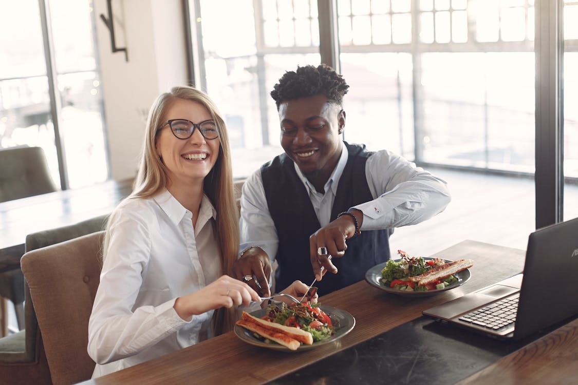 Cheerful diverse coworkers eating together in cafe