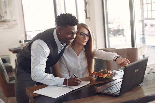 Young diverse entrepreneurs in formal clothes sitting in modern cafe with laptop and planner while working on project together during lunch break