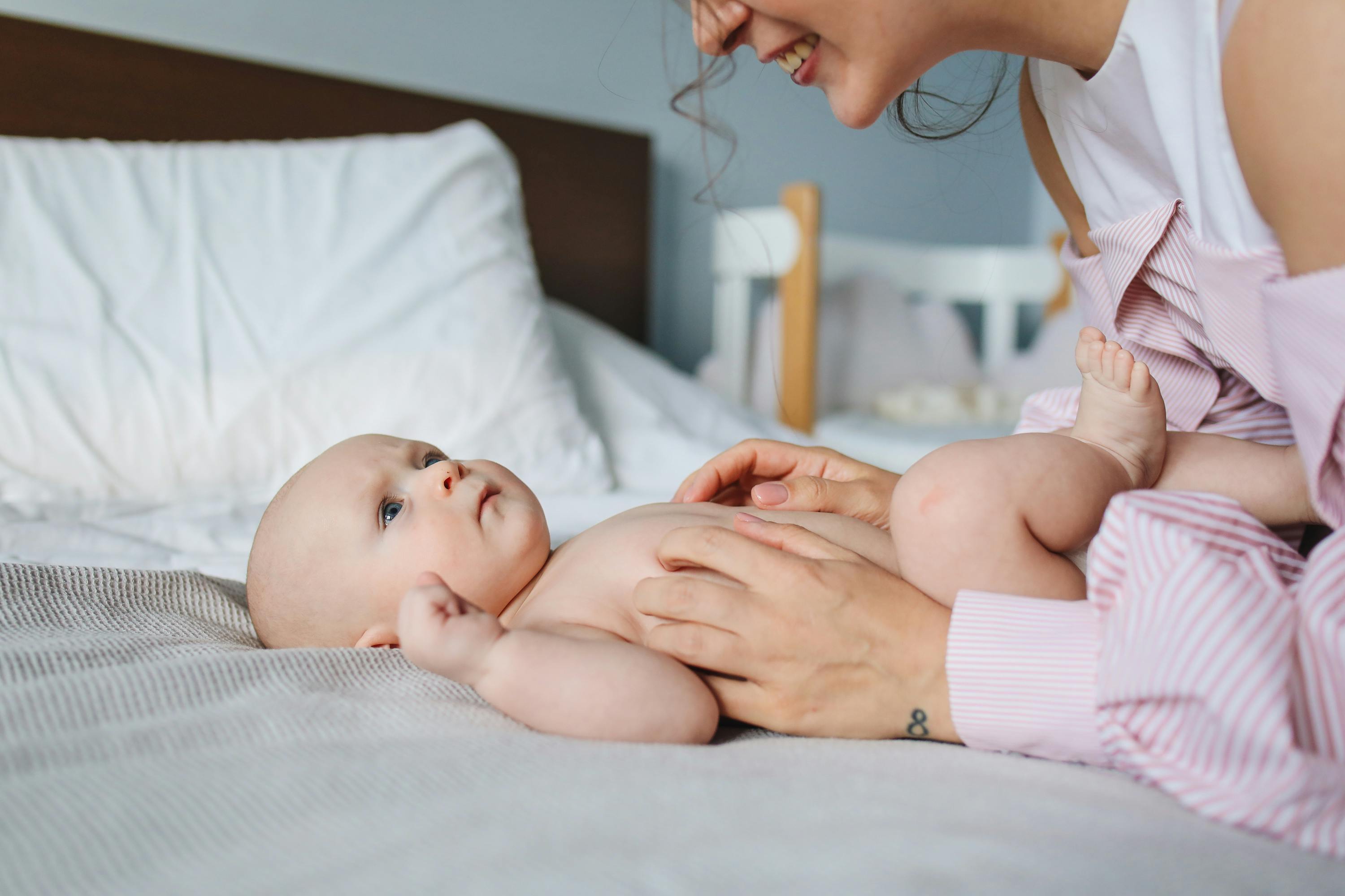 woman in white and pink striped long sleeve shirt playing with baby lying on bed