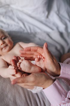 特写镜头中，父母的手在室内床上轻轻握住婴儿的脚