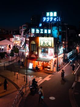 Vibrant Tokyo street scene at night featuring illuminated signs and people enjoying the urban atmosphere.