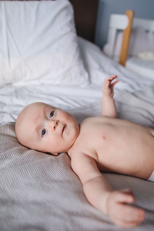 Free A cute baby relaxing on a bed in a softly lit bedroom, showcasing innocence and calm. Stock Photo