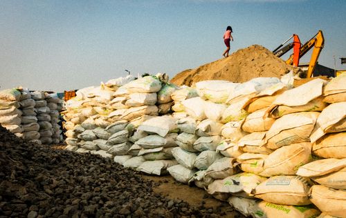 Free Image of a construction site with stacked bags, heavy machinery, and a child on a dirt mound. Stock Photo