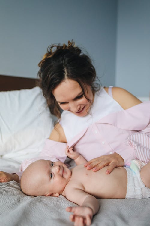 Free  Woman in Pink Top Touching Baby Lying on Bed Stock Photo