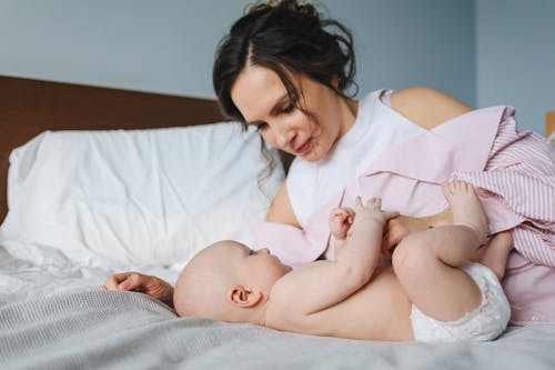 Free Woman in White and Pink Striped Long Sleeve Shirt Playing with Baby Lying on Bed Stock Photo