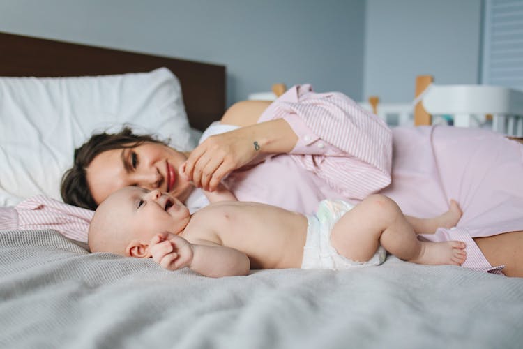 Mother Lying Down On Bed Next To Her Baby