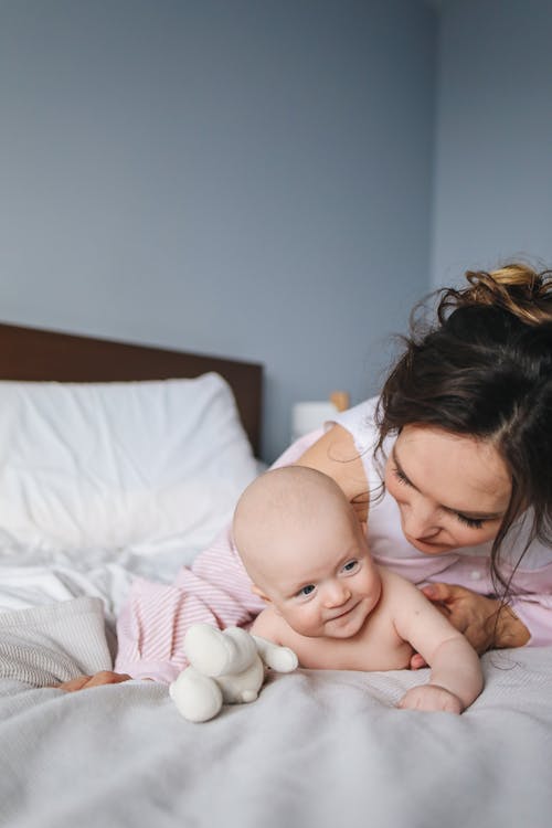 Free Woman in White and Pink Top Playing with Baby Lying on Bed Stock Photo