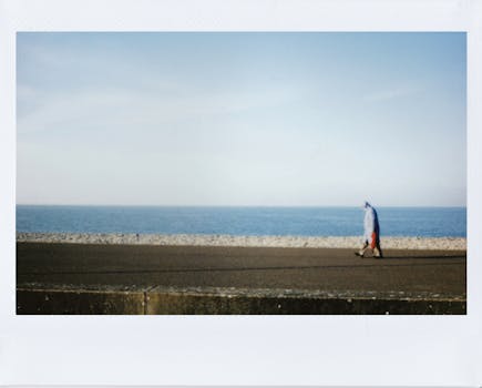 一个人沿着海滨长廊散步，头顶是晴朗的蓝天