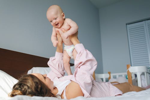 Free Mother Lying Down on Bed while Carrying Her Baby Stock Photo