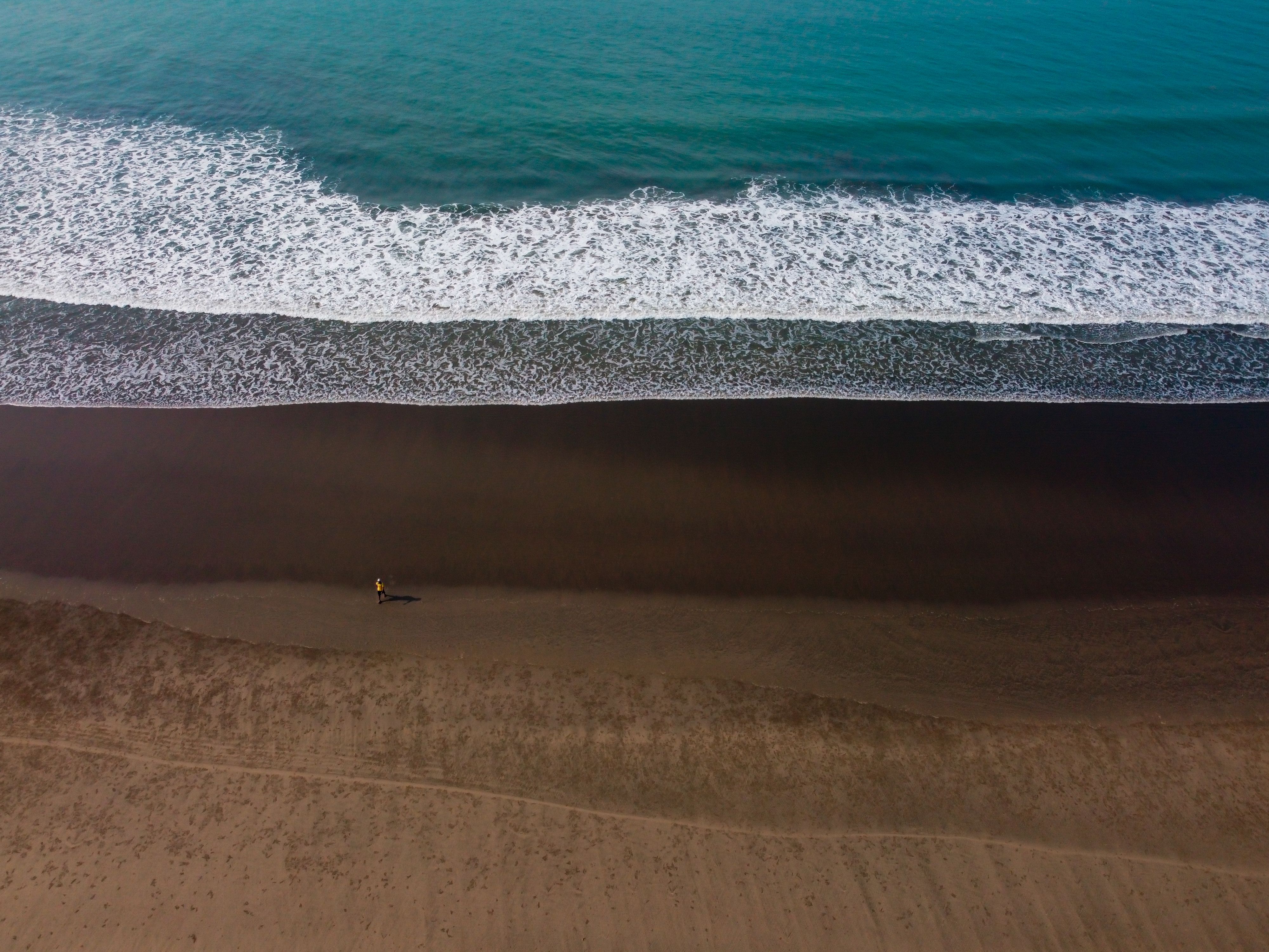 Aerial perspective of Cox's Bazar, capturing serene waves and a solitary beach walker.