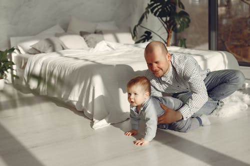 Adorable child with father playing in bedroom while spending time at home together at morning wearing casual clothes looking away